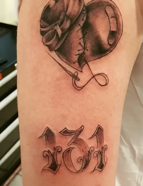 Tatuaje de corazón cosido con aguja e hilo y el número 131 en letra ornamental