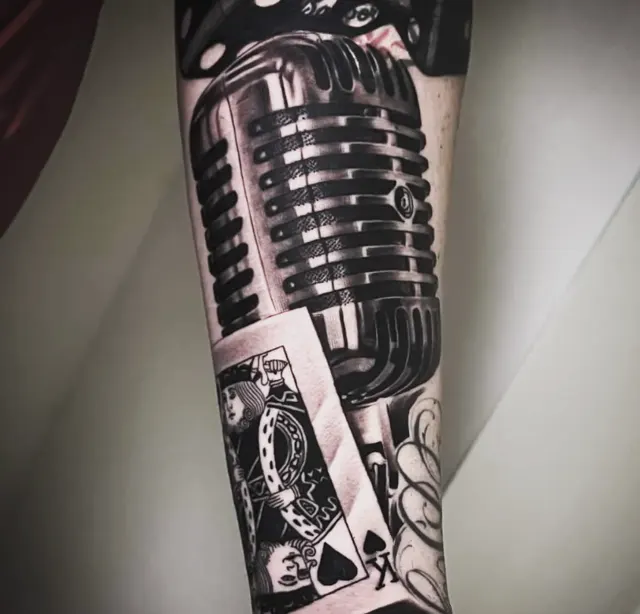 Tatuaje en antebrazo: micrófono vintage cromado y carta del rey de espadas en negro y gris